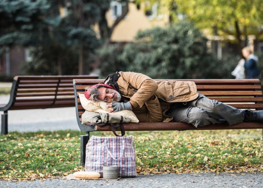 Older man experiencing homelessness sleeping on a bench