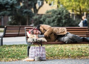 Older man experiencing homelessness sleeping on a park bench