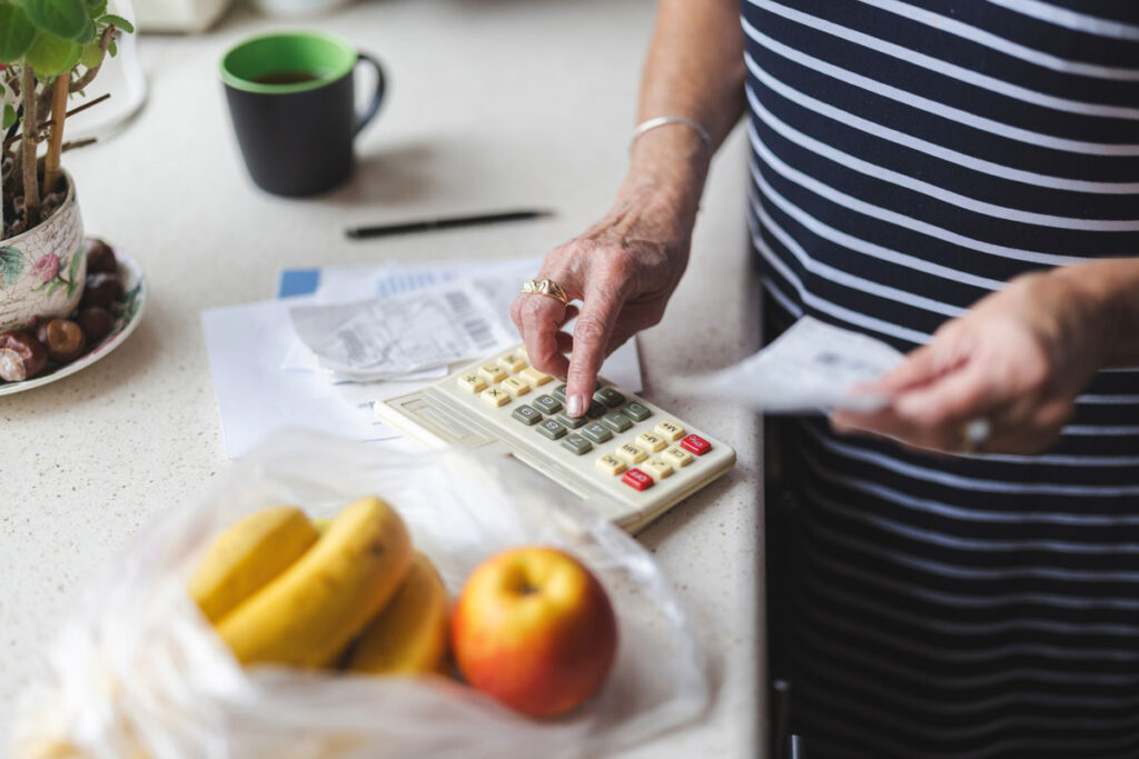 Woman using a calculator to track receipts with bananas and an apple in the foreground.